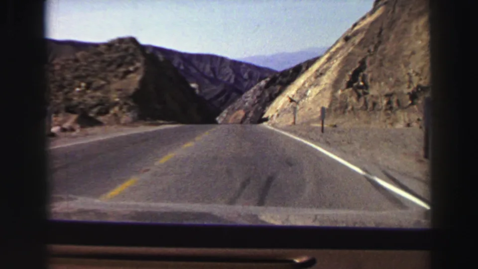 The vehicle approaches a bend on a Lake Tahoe-area mountain highway, with rocky cuts and blue ridges visible ahead.