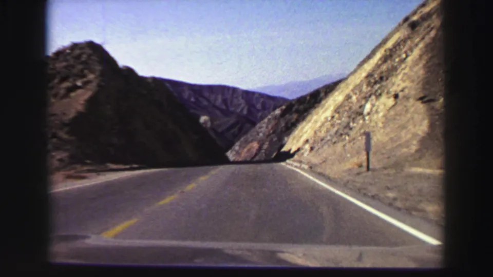 A passenger-facing windshield view shows a 1969 Lake Tahoe-area road narrowing visually between steep dry slopes.