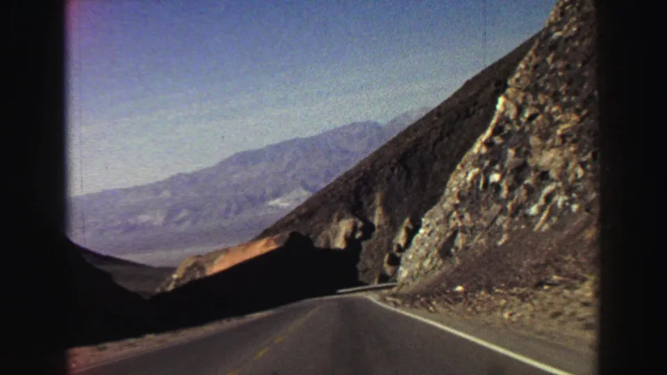 Vintage 8mm view of a Lake Tahoe-area mountain road curving past a steep rock face, filmed from inside a moving car in 1969.