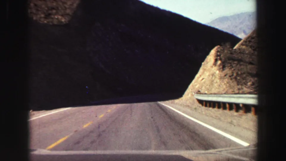 Lake Tahoe-area 8mm road footage from 1969, showing a moving-car view through a shadowed rocky pass with guardrail and distant light.