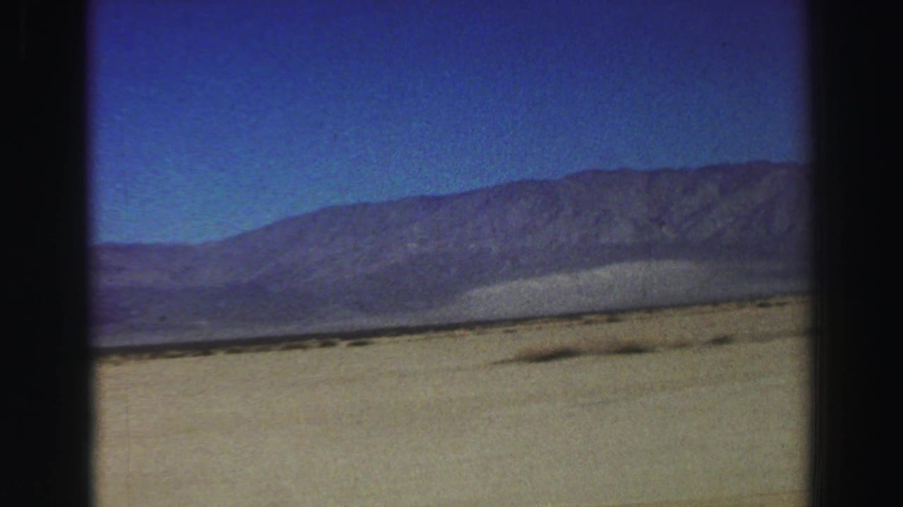 Dry open plain with distant mountains under a deep blue sky, seen through dark film-frame borders.