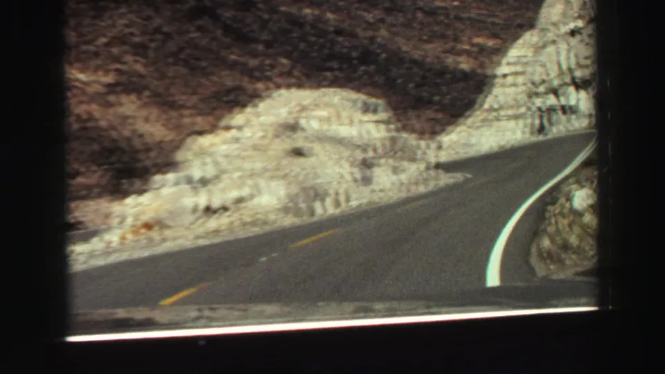 1969 Lake Tahoe area road view with asphalt curving along pale rock formations, seen from a moving vehicle perspective.