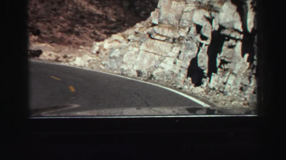 Lake Tahoe-area road footage from 1969 shows the car approaching a bend with exposed rock faces and painted lane markings ahead.