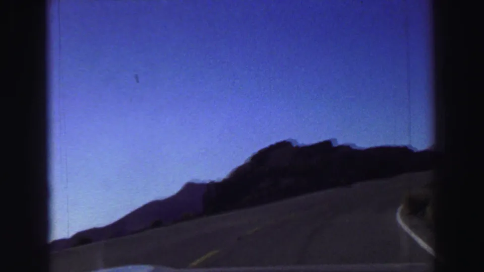 Lake Tahoe road-trip footage shows a two-lane road curving beside dark rocky terrain under clear sky.