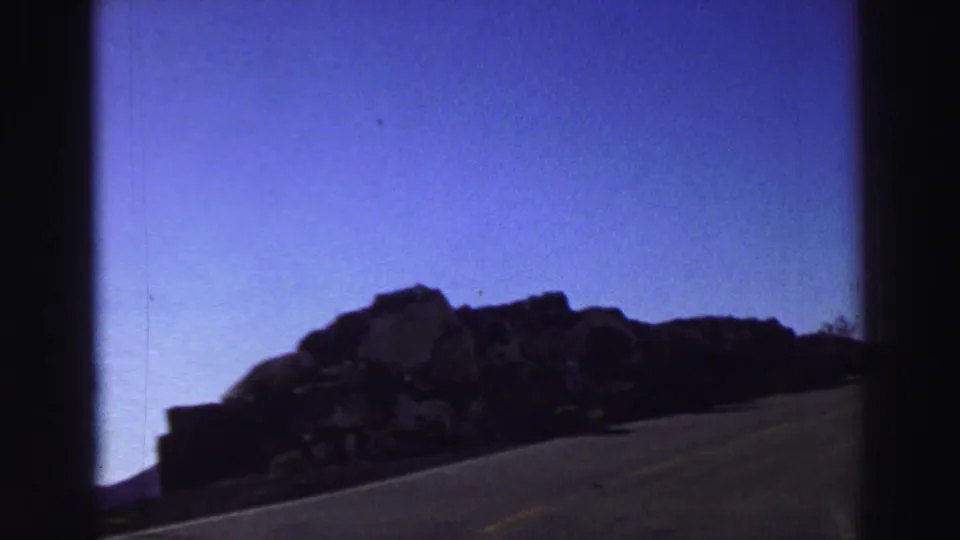A moving-car view passes a rocky roadside outcrop along a Lake Tahoe mountain road in 1969 footage.
