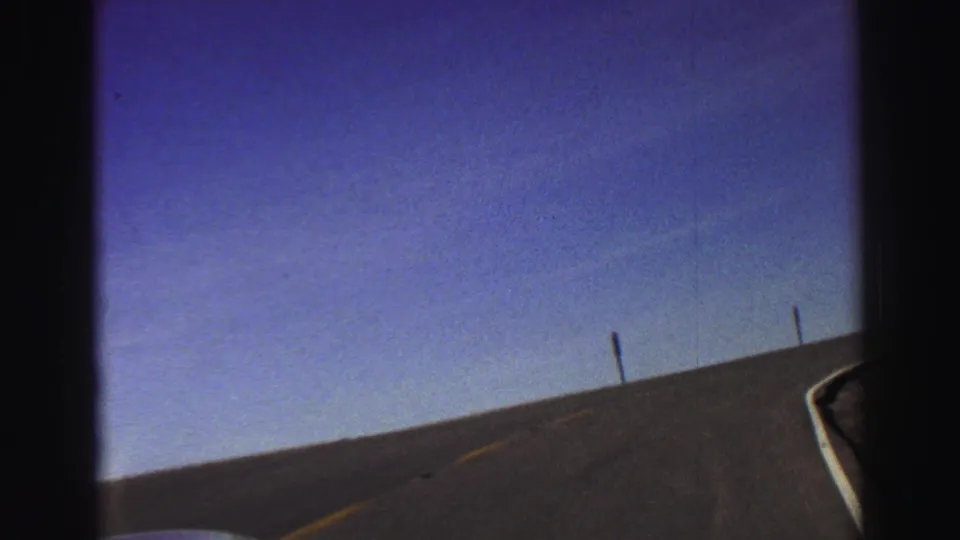 Late-1960s 8mm Lake Tahoe road footage showing an open uphill curve, roadside markers, and a clear blue sky.