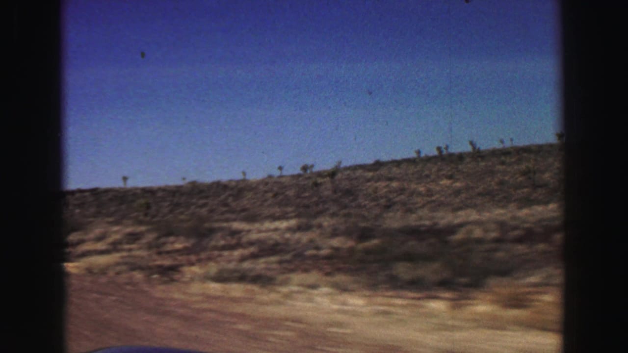 Dry hillside with sparse scrub seen from a moving vehicle under blue sky.
