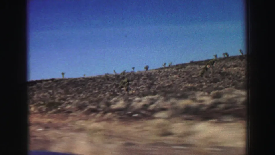1969 8mm passenger view of dry California hillside and roadside brush, softened by vehicle motion.
