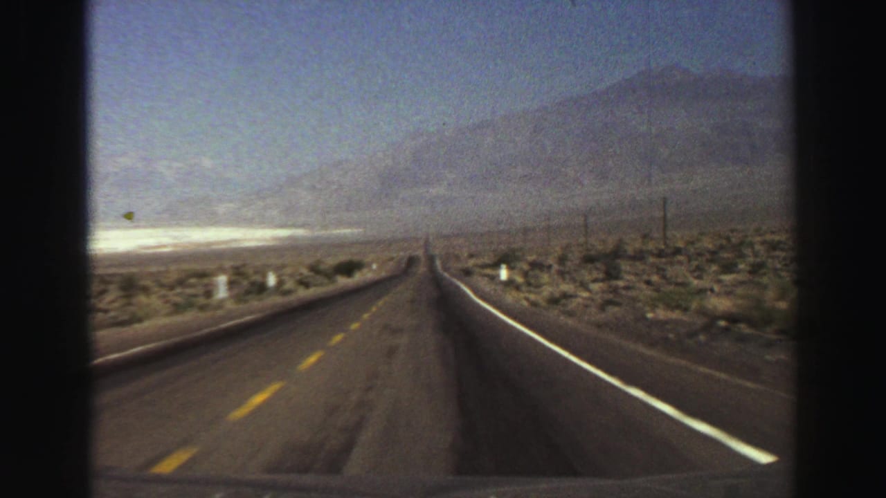 Straight desert road leading toward distant mountains under a hazy blue sky.