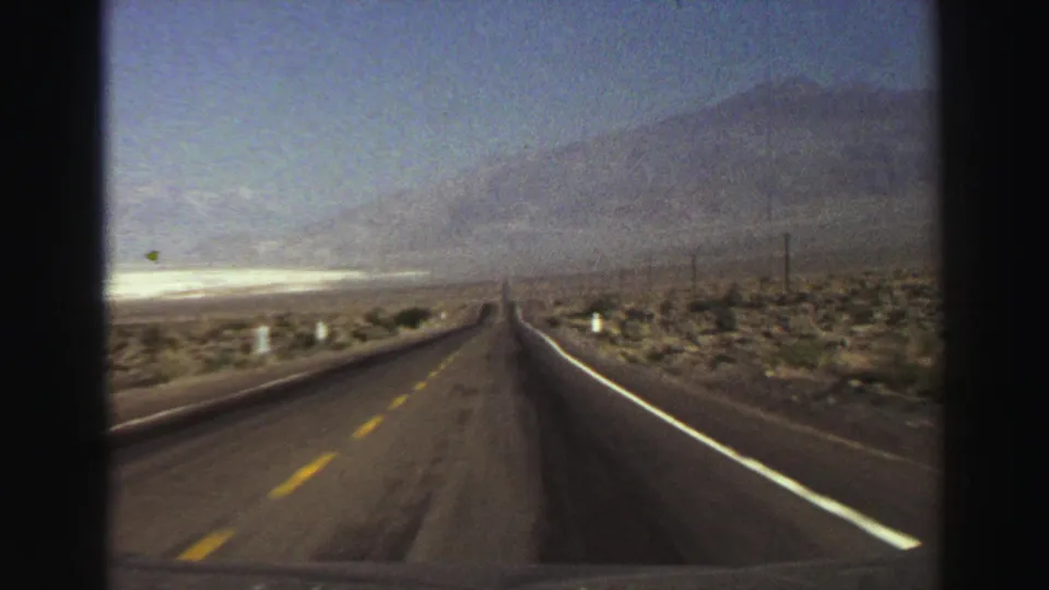 1969 8mm road-view footage in the Lake Tahoe, California metadata context, showing a straight highway through arid terrain toward mountains.