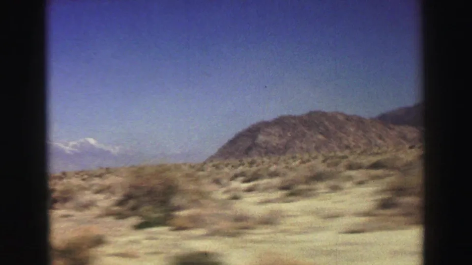 1969 8mm moving-vehicle view near Lake Tahoe, showing scrubby open ground, a low hill, and distant pale mountains.