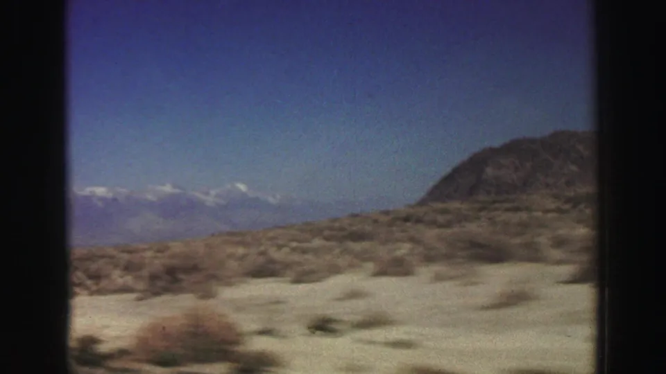 1969 8mm Lake Tahoe-area landscape frame with sandy scrubland, a rocky hill, and hazy mountains in the distance.