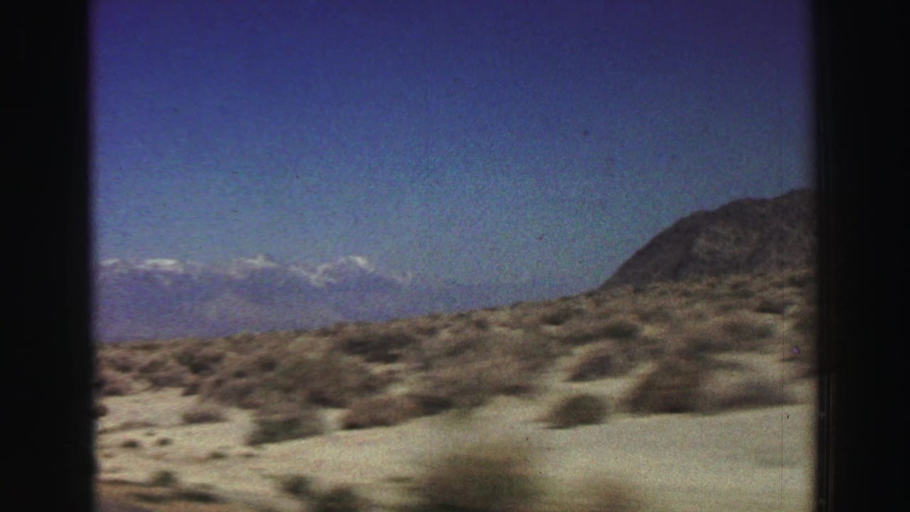 Desert scrub and distant snow-capped mountains seen through dark vehicle-window edges.