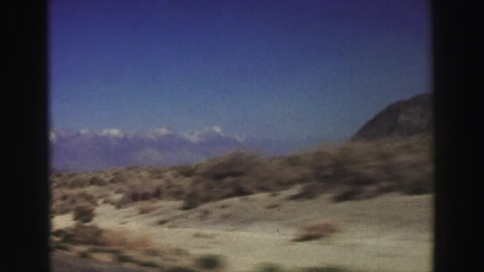 A fast passenger-window view shows scrubland and distant snow-capped mountains in the Lake Tahoe, California travel clip.