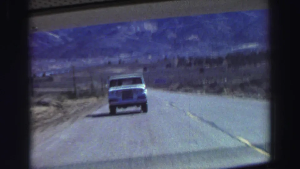 8mm road-trip frame showing a light truck ahead as the highway bends through a rugged Tahoe-region landscape.