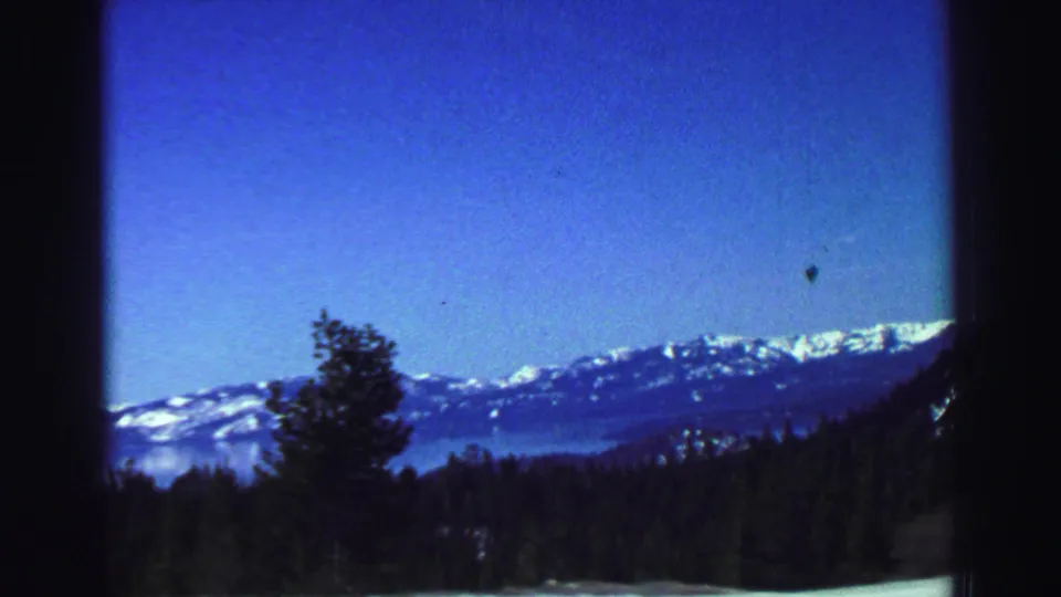 Scenic 1969 Lake Tahoe-area home-movie view of a lake, evergreen foreground, and snow-capped mountain ridge.