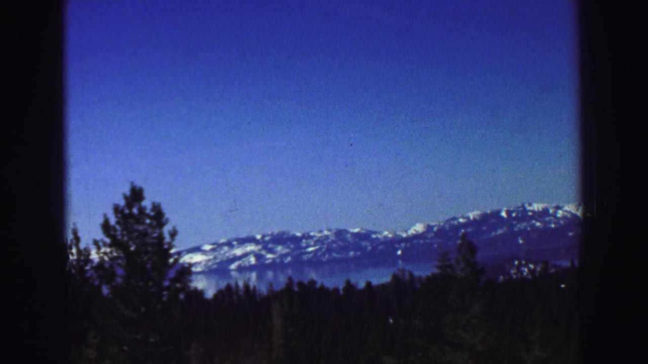 Lake Tahoe-area mountains and pine forest appear under blue sky, with dark in-camera framing from the home-movie viewpoint.