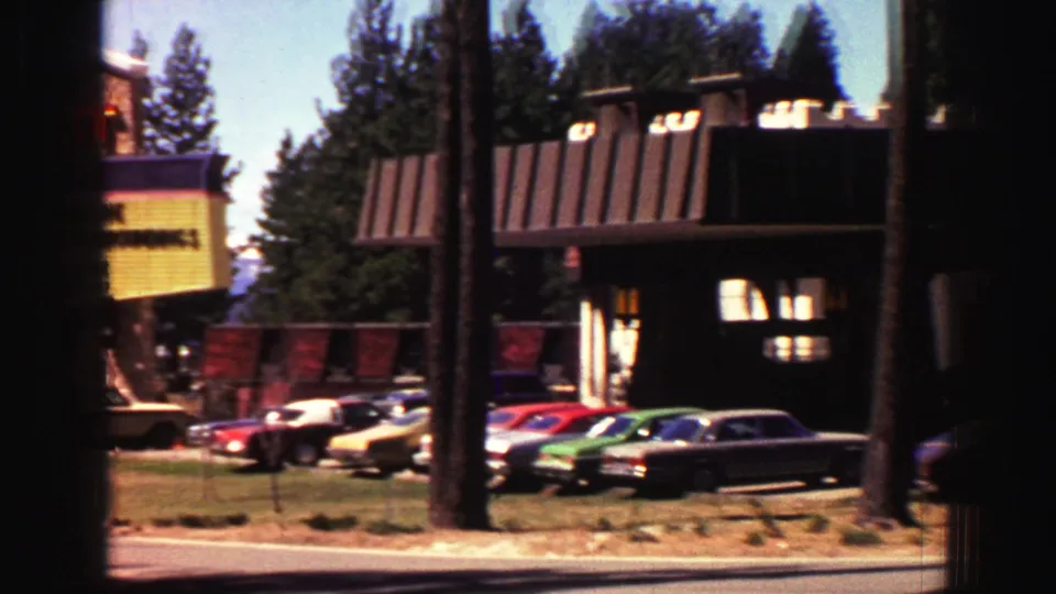 Lake Tahoe hotel exterior with mid-century parked cars, dark timber facades, and tall pines in bright daylight.