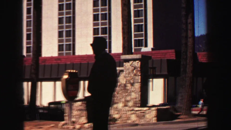 Silhouetted man in a hat stands near stone entry pillars outside a Lake Tahoe hotel in the supplied 1969 footage.