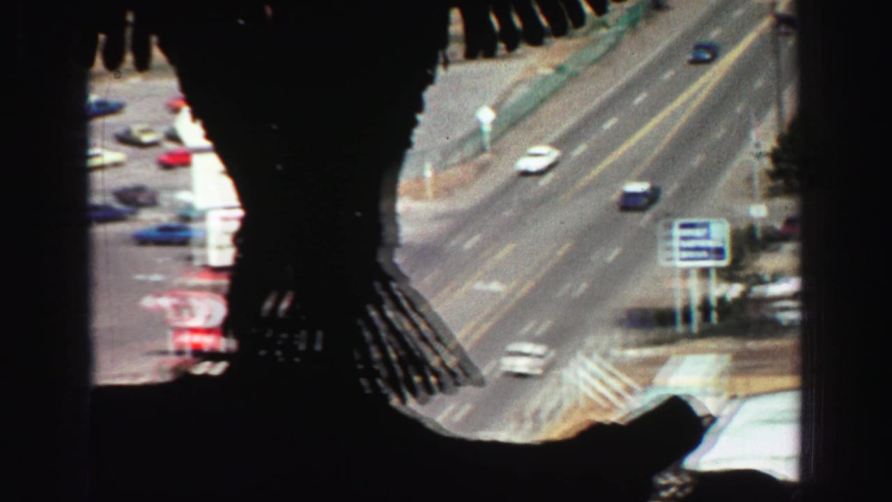 Silhouetted passenger shape beside a high-angle view of a multi-lane road and moving cars.