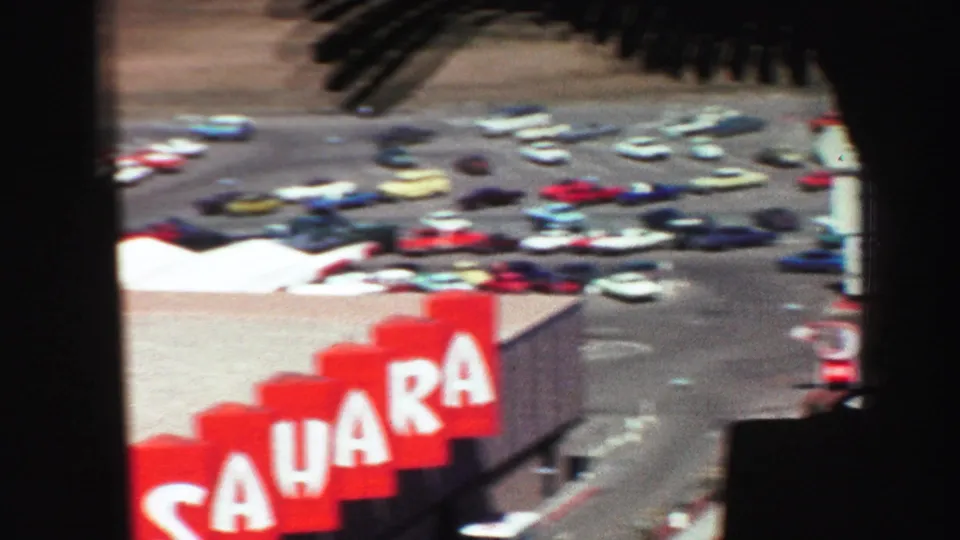 Elevated 1969 city view showing many parked cars and a prominent red Sahara sign seen through dark window framing.