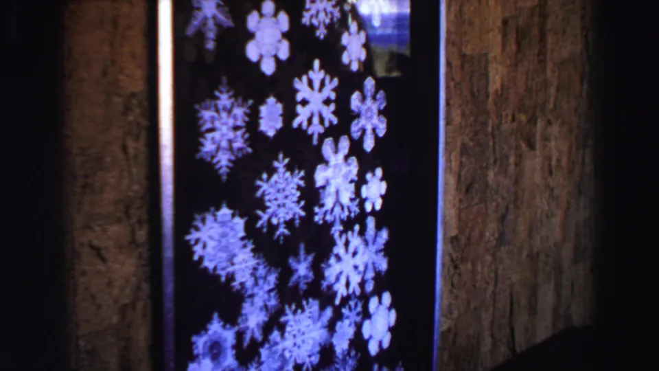 1969 Lake Tahoe home-movie frame with a snowflake-patterned window or display near a textured interior wall.