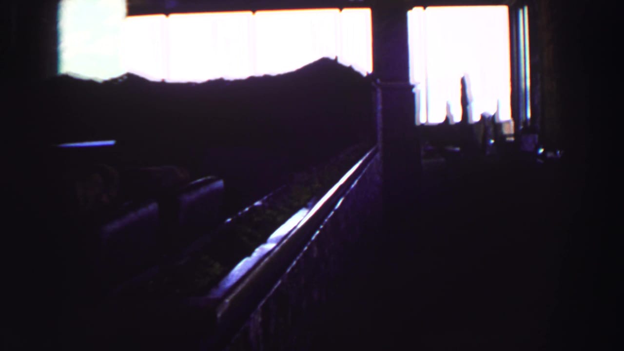 Dark interior looking toward bright windows with a silhouetted bed or seating area.