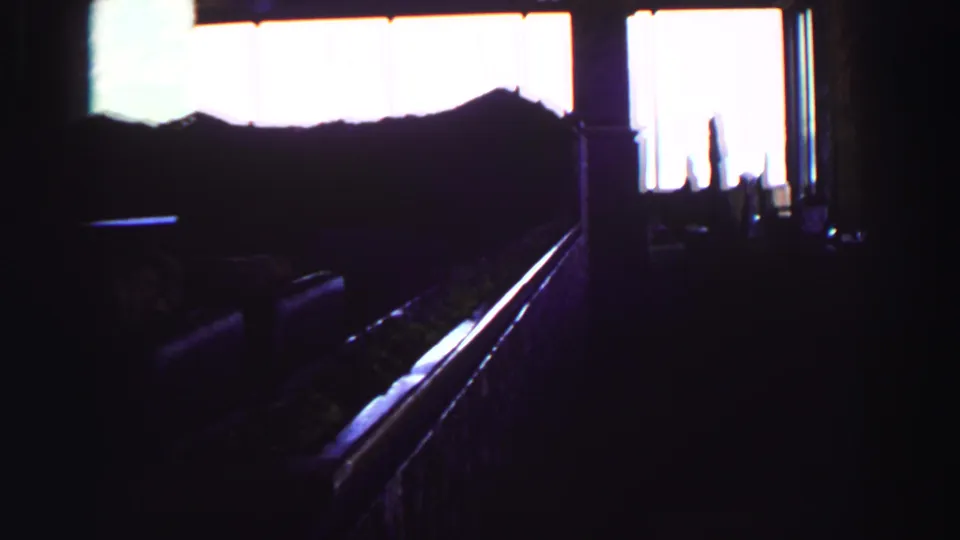 Underexposed 1969 home-movie frame from Lake Tahoe, looking from a dark interior toward bright windows and a silhouetted room edge.