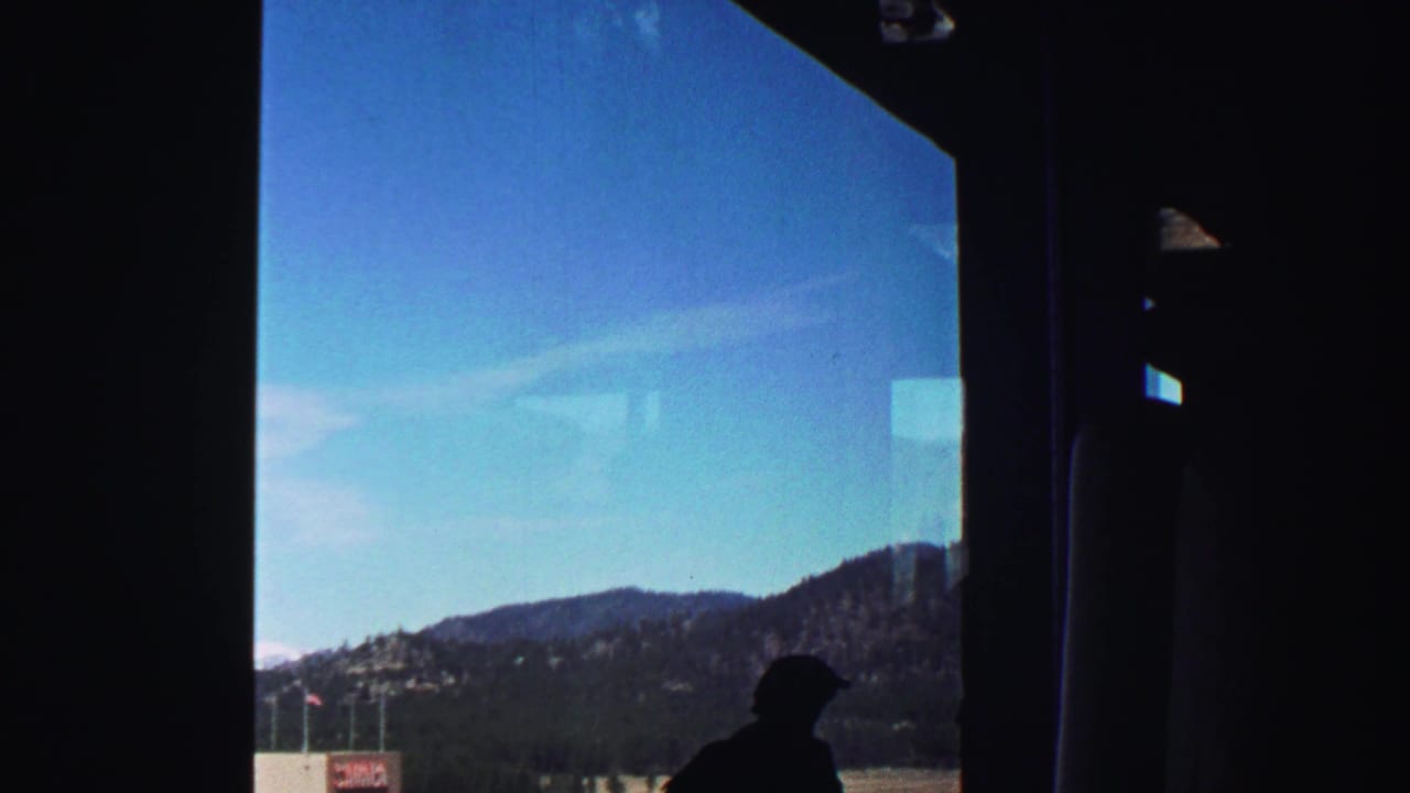 Silhouetted passenger inside a vehicle looking toward wooded hills through a window.