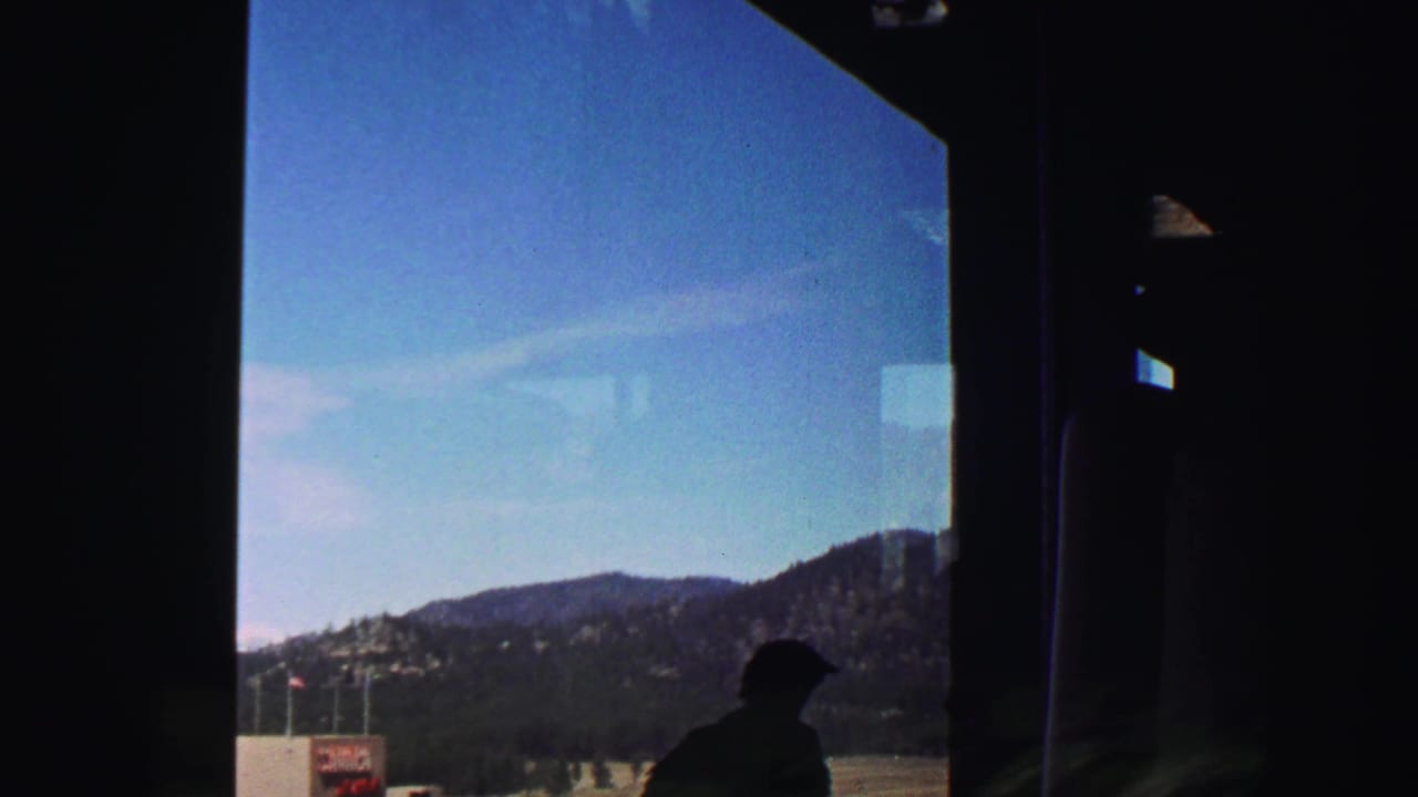 Dark vehicle interior framing a passenger silhouette with mountains and sky outside.