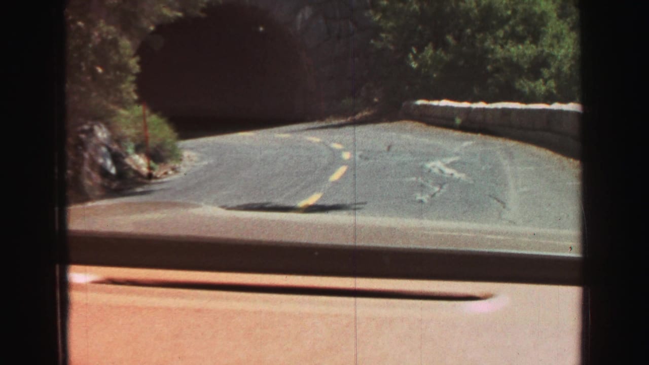 Vehicle windshield view of a curving road approaching a stone tunnel.