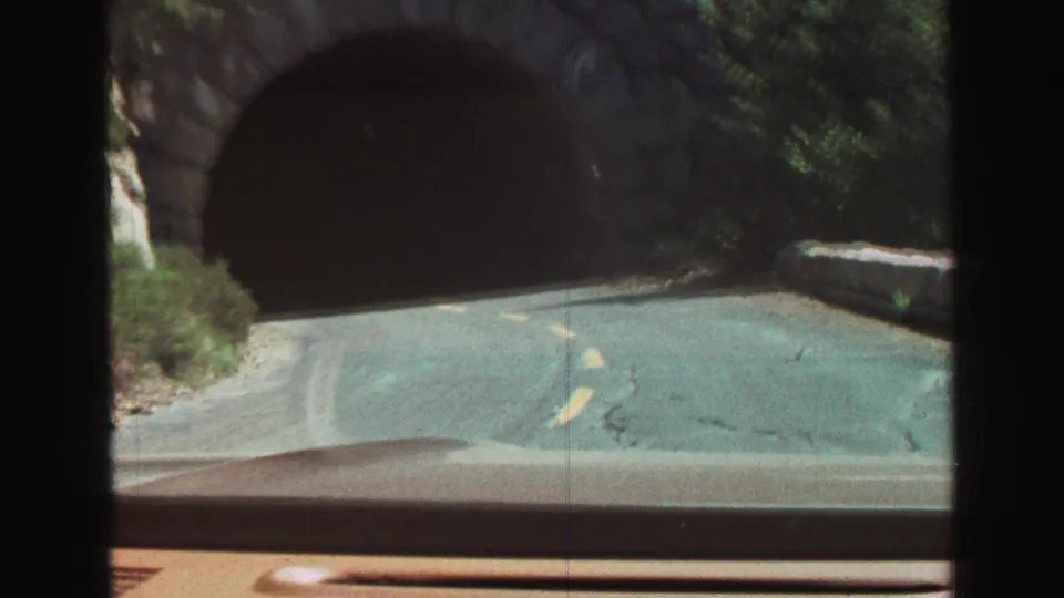 The dashboard-level 8mm view closes in on the dark tunnel entrance as the road markings lead into the stone arch.