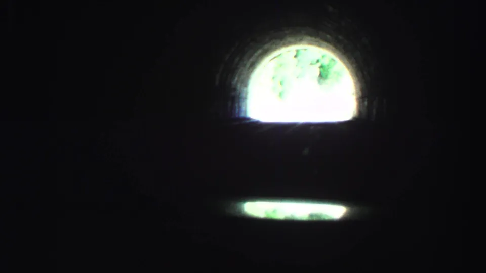 First-person 8mm driving view in a Lake Tahoe tunnel, with a bright arched exit and a dim reflection below.