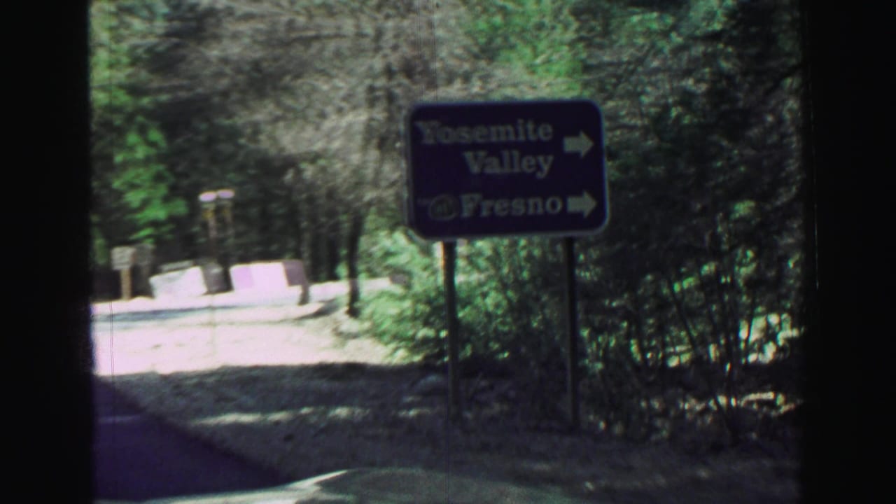 Road sign for Yosemite Valley and Fresno beside a forest road.