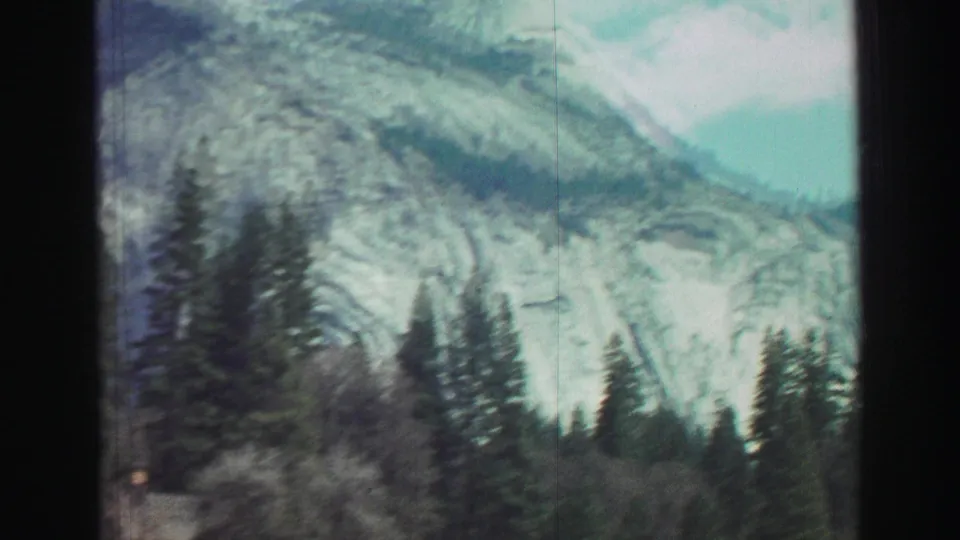 Soft 1969 Lake Tahoe-area 8mm frame showing evergreen trees and pale mountain rock faces blurred by motion from the moving vehicle.