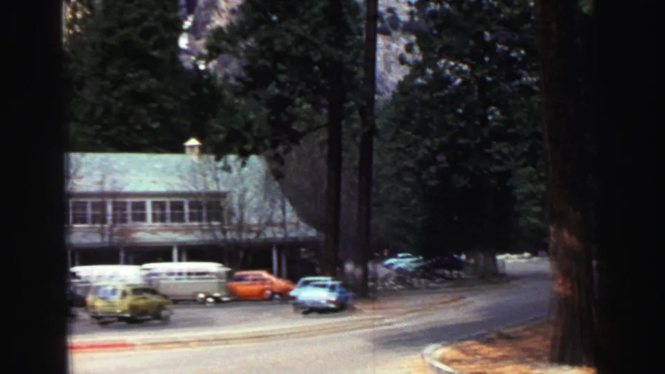 A lodge-like roadside building and several parked cars sit among tall trees in the Lake Tahoe mountain setting.