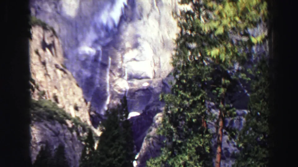 1969 8mm mountain scenery near Lake Tahoe, with evergreens in front of cliffs and a waterfall dropping through the rock.