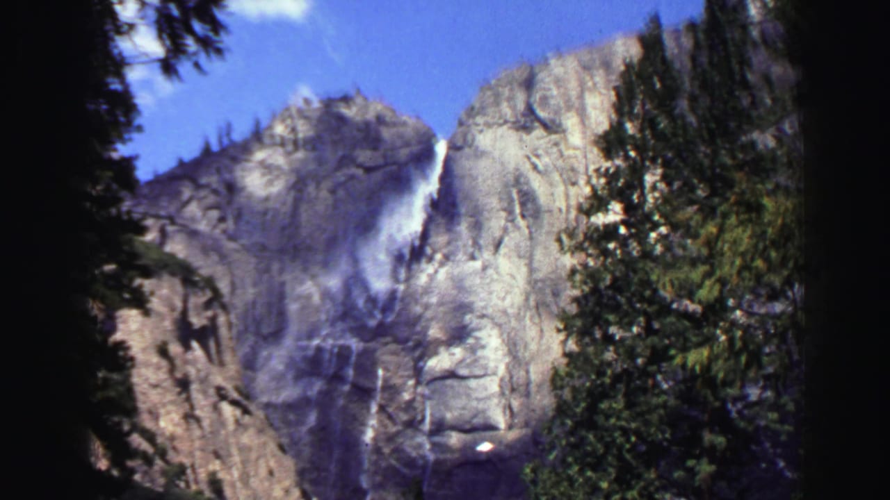 1969 Lake Tahoe 8mm frame showing a waterfall on a granite cliff, partly framed by evergreen trees and dark film edges.