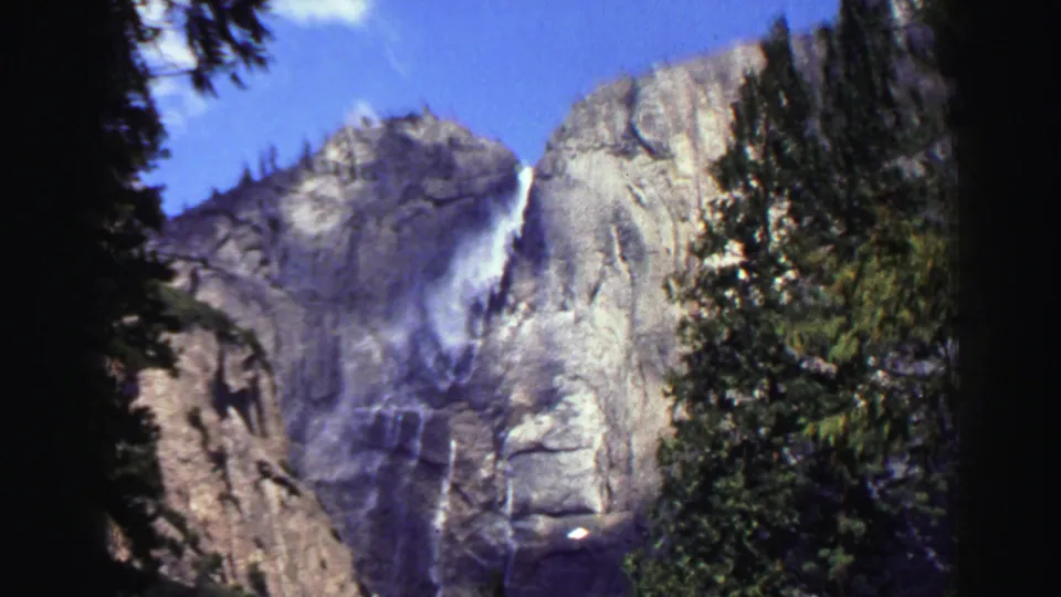 1969 Lake Tahoe 8mm frame showing a waterfall on a granite cliff, partly framed by evergreen trees and dark film edges.