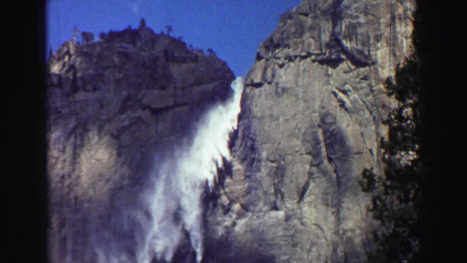 1969 Lake Tahoe 8mm frame showing the waterfall plume beside a large granite face, with conifers and dark film edges in view.