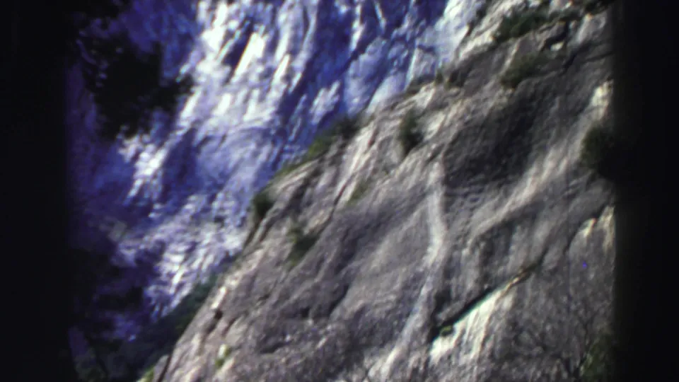 Soft, handheld 8mm Lake Tahoe frame of a granite mountain face with nearby tree silhouettes and heavy shadow at the edge.