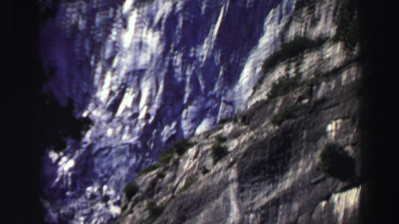 Granite cliff face partly framed by dark pine silhouettes and blue sky.