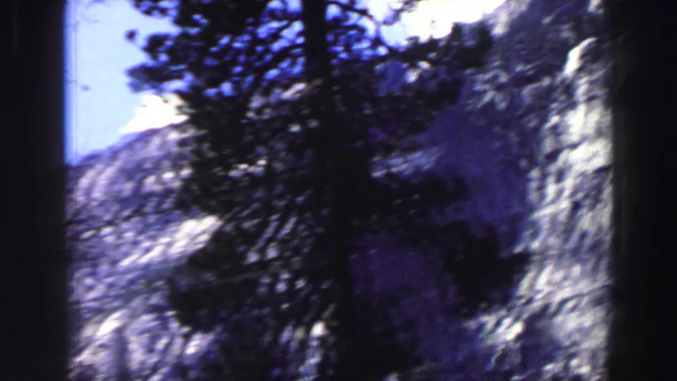 1969 Lake Tahoe 8mm frame with handheld blur across pines, shaded forest shapes and a pale granite cliff.