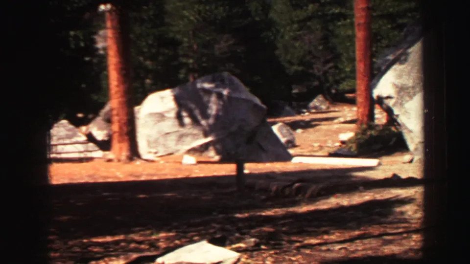1969 Lake Tahoe vacation footage showing a picnic table near granite boulders and tall pine trunks in a shaded park area.