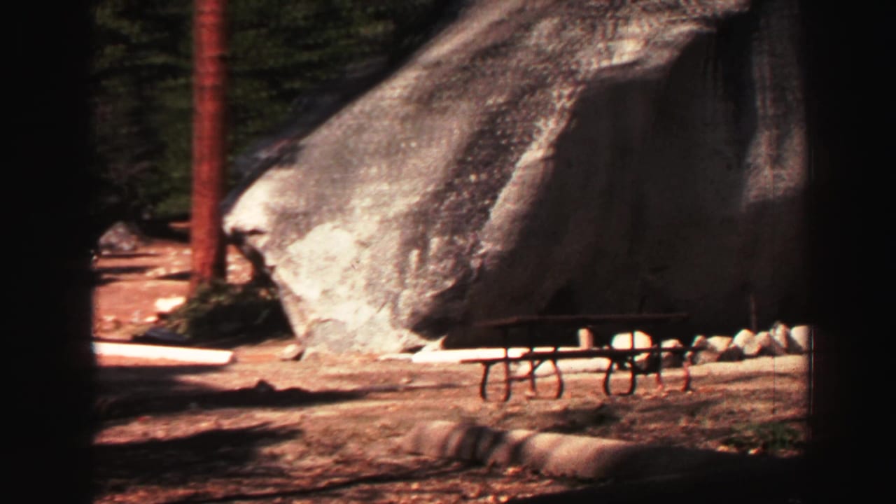 1969 Lake Tahoe 8mm frame showing a picnic table below a massive granite boulder in a wooded campsite.