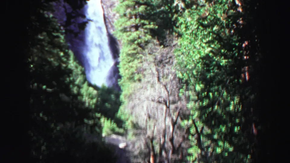 A tall waterfall descends past a rocky cliff in the Lake Tahoe area, framed by dense trees and soft 8mm color.
