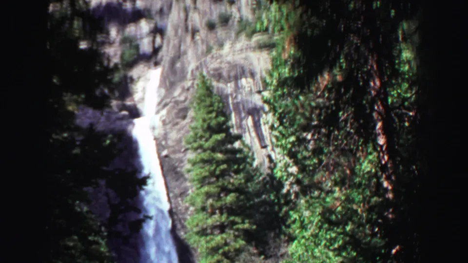 The camera holds on a tall waterfall cascading down a rocky, tree-lined slope in 1969 Lake Tahoe travel footage.
