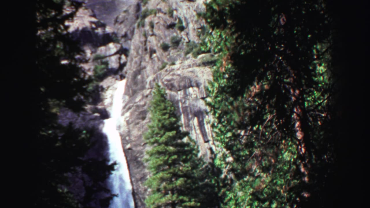 Waterfall dropping down a rocky cliff among evergreen trees.