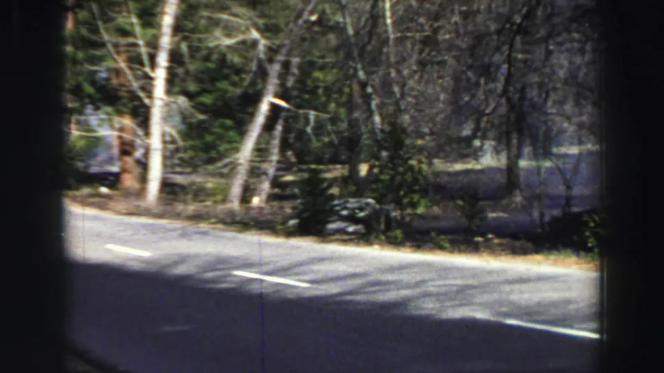 1969 Lake Tahoe-area home-movie frame of a wooded two-lane road viewed from inside a moving vehicle.