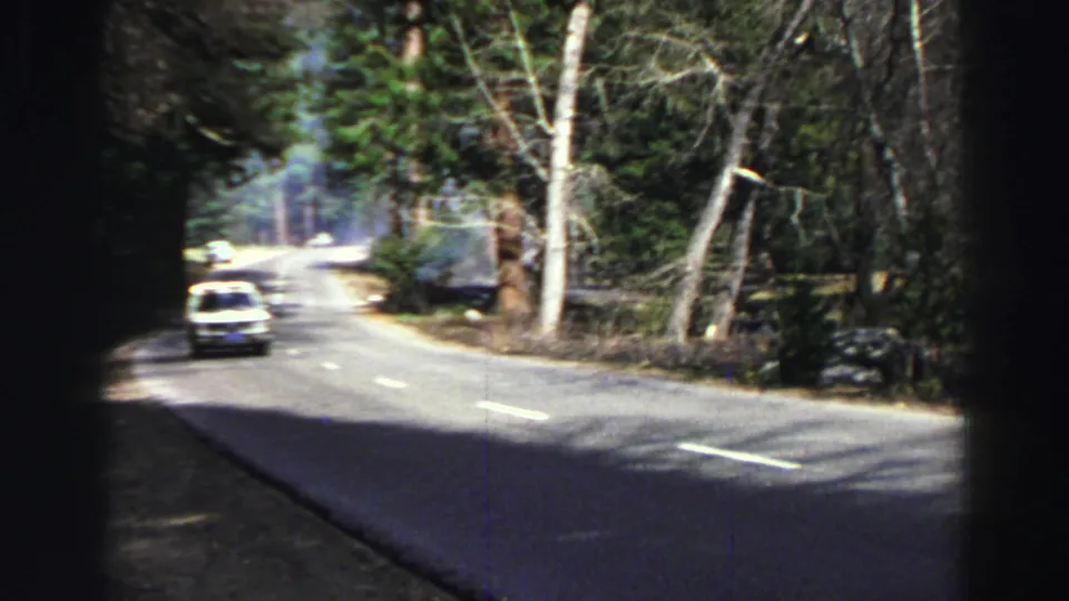 A white car approaches on a forest road near Lake Tahoe in this 1969 8mm travel footage frame.